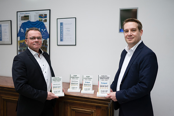 Two employees in suits smilingly present the awards for Knüppel and Excor.